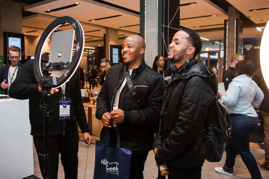 Two event guests stand beside a ring light and tablet capture station.